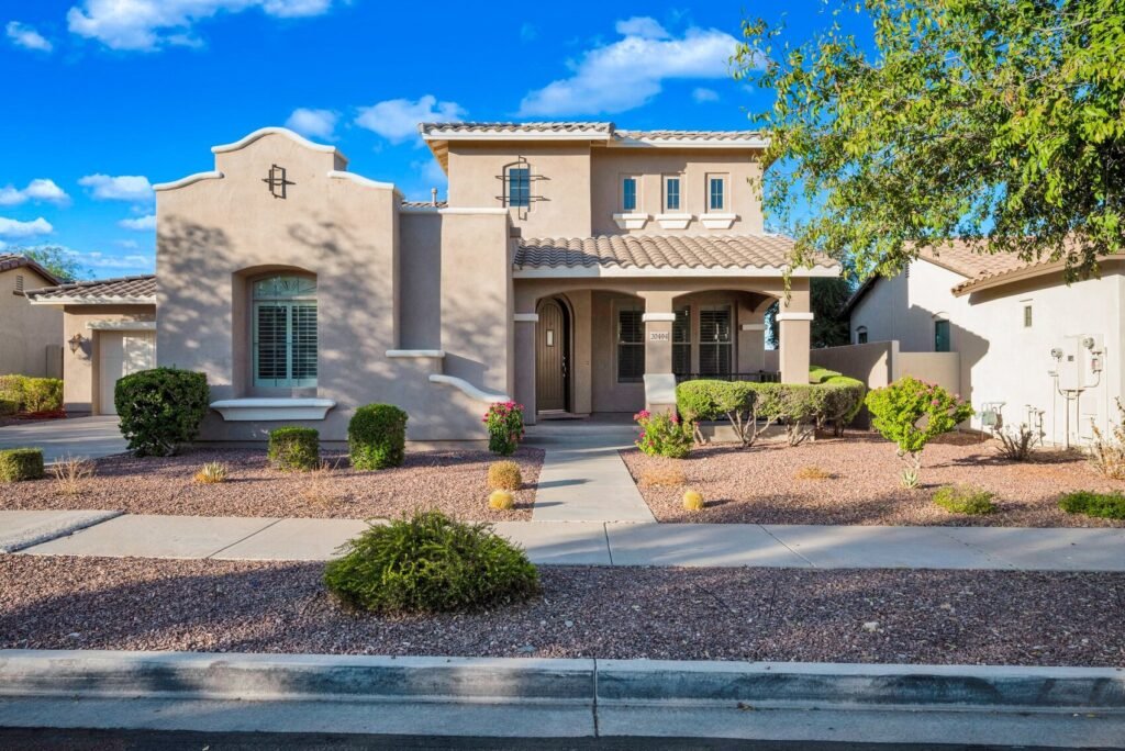 The image showcases a well-maintained home characterized by its Southwest architectural style. The structure features a warm, sandy exterior color, which reflects the sunlight beautifully against the backdrop of a bright blue sky dotted with fluffy clouds.