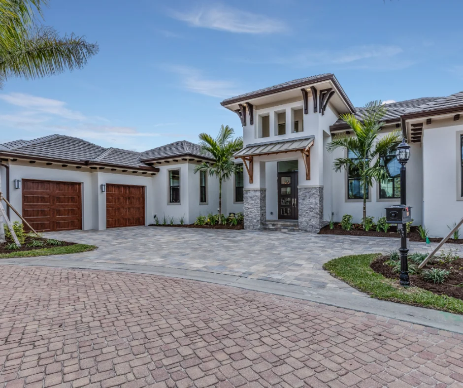 Luxury modern home with stone accents, wood garage doors, palm trees, and a paved driveway.